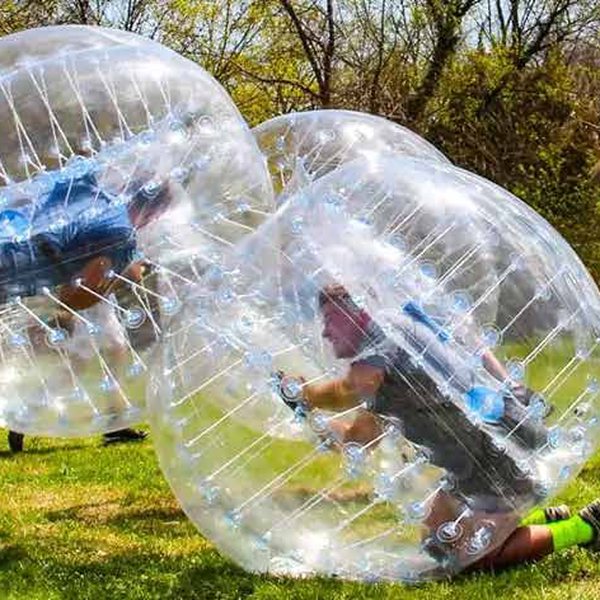 Players inside clear inflatable bumper balloons on grass