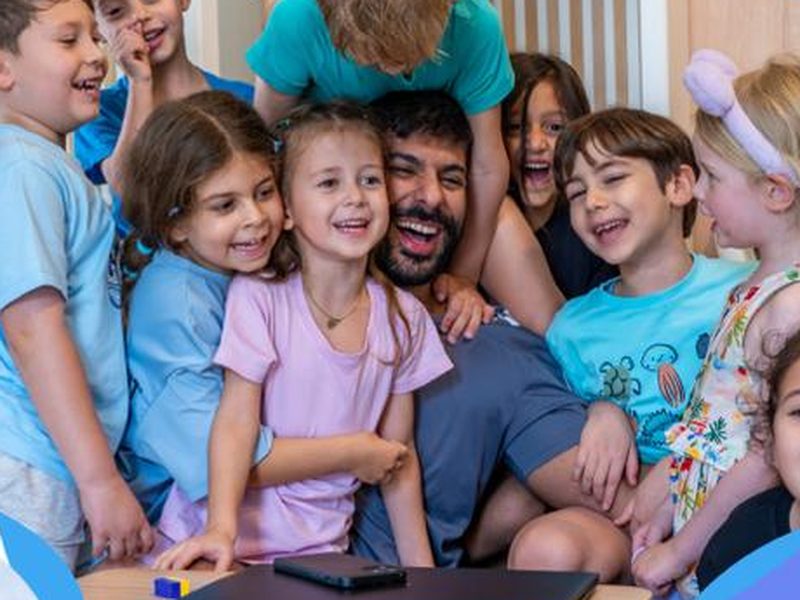 Laughing children crowding around their coach at the La Folie camp at HandPrint, Umm Suqeim, Dubai